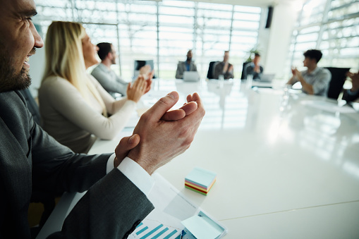 Close up of happy businessman and his colleagues applauding on a successful meeting in conference room. Copy space.