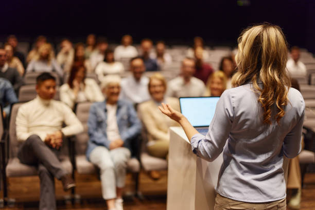 Vista posteriore di un oratore femminile che tiene un discorso di fronte alle persone al centro congressi. - foto stock