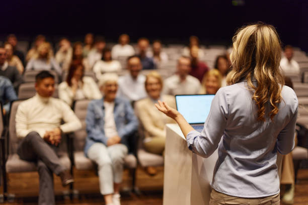 Cтоковое фото Вид сзади на женщину, выступающую с речью перед людьми в конференц-центре.