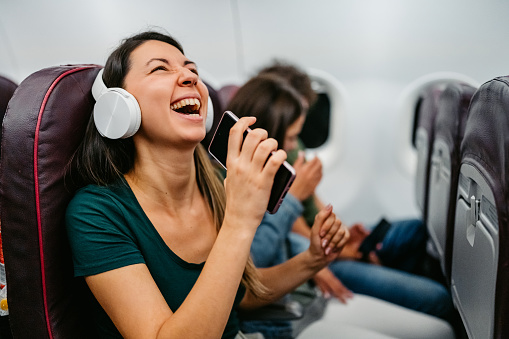 Beautiful young woman listening to music via headphones using her smart phone in an airplane.