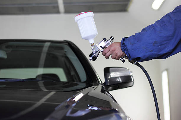 Hand holding a spray paint gun pointed at a black car