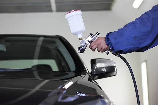 Photo of Hand holding a spray paint gun pointed at a black car