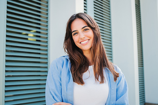 Happy caucasian young student female looking at camera enjoying with a perfect white teeth. Portrait of a joyful and adorable teenage brunette woman posing for a college promotion with crossed arms. High quality photo