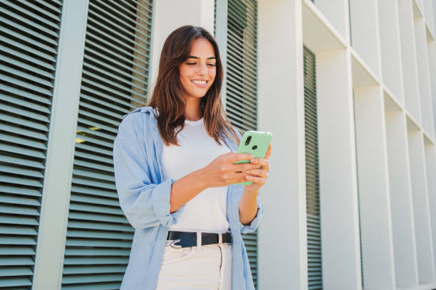 istock Smiling young woman using mobile phone app , texting, playing game, shopping online, ordering delivery. Happy millennial teen girl sharing social media holding smartphone outdoors. 1759458983