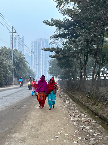 Noida, Uttar Pradesh, India - January 09, 2023: Stock photo showing women wearing traditional clothing walking along the side of a busy road during cold, frosty weather.