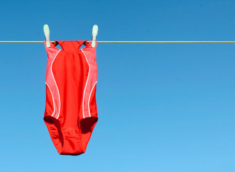 A red swimsuit hanging on a clothesline drying in the sun.