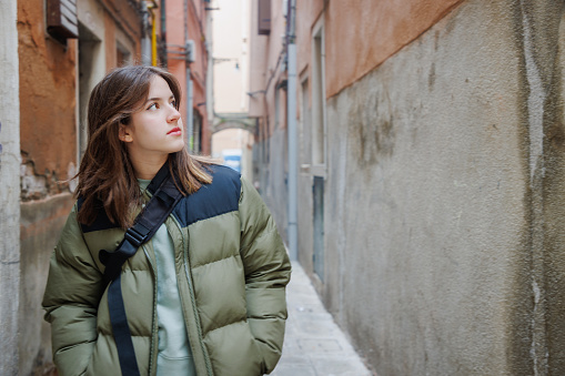 Portrait of beautiful teenage girl standing in the narrow street between old buildings and looking away, visiting Venice in Italy