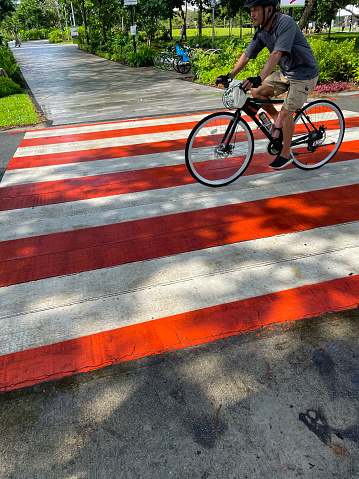 East Coast Park, Singapore - February 11, 2023: Stock photo showing close-up view of cyclist riding over striped zebra road crossing with red and white painted road markings on tarmac surface.