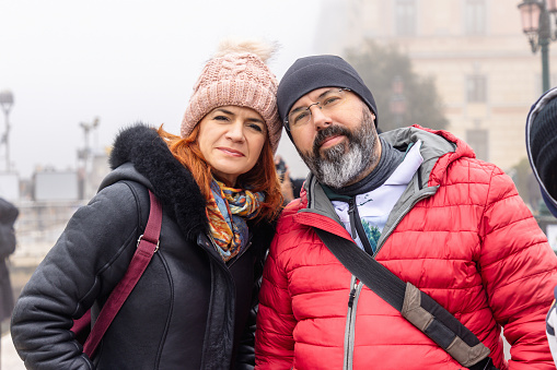 Beautiful middle aged married couple in warm clothing looking at camera, foggy day in winter, visiting Venice in Italy together