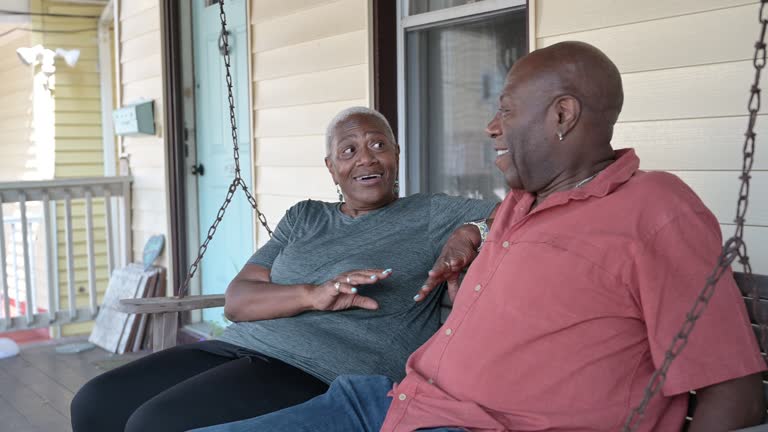 Cheerful retirees sitting on porch swing and talking