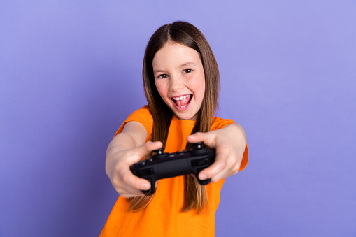 Photo of funky schoolkid with straight hairdo dressed orange t-shirt play videogame hold joystick isolated on purple color background.