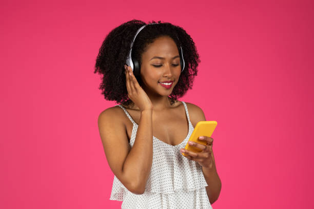 glückliche millennial-afroamerikanerin lockige dame in kabellosen kopfhörern, die musik hört und auf dem smartphone tippt - internet dating audio stock-fotos und bilder