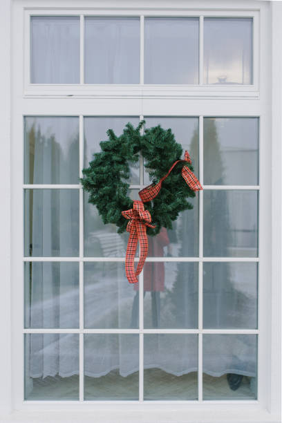 istock Christmas wreath with a red bow on a white window in a private house 1759495091