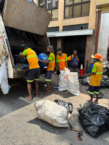 Colombo, Sri Lanka - January 10, 2023: Stock photo showing residential street with refuse collection team gathering rubbish to toss into the open back of a garbage lorry.