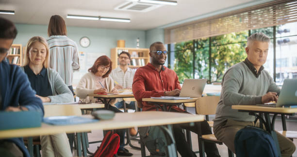 istock Adult Education Center: Diverse Mature Students Learning in Classroom, Using Laptop Computers and Writing in Notebooks. Group of People Taking a Workshop on Improving Professional Work Skills 1759499529