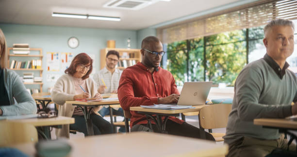 istock Adult Education Center: Diverse Mature Students Learning in Classroom, Using Laptops and Writing in Notebooks. Group of People Taking a Workshop on Improving Professional Work Skills 1759500058