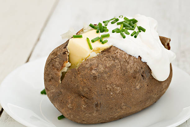 Baked Potato With The Works A high angle close up shot of a baked russet potato with butter, sour cream and chives. baked potato sour cream stock pictures, royalty-free photos & images