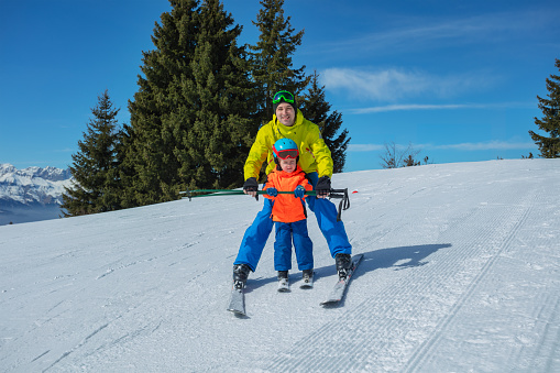 Instructor teaches little kid skiing gliding behind holding ski poles together with hands showing snowplow wedge move
