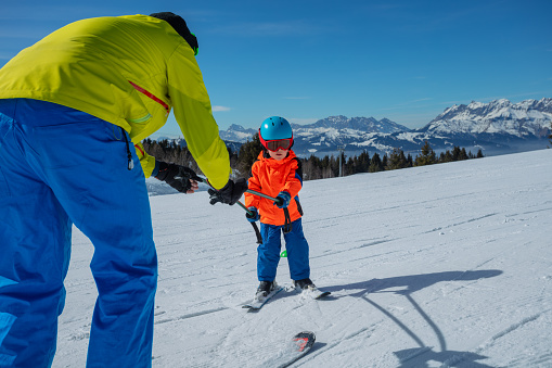 Dad teach little boy child to ski on the alpine slope by rolling below and holding poles