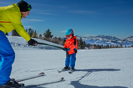 Man teach little boy child to ski on the alpine slope by rolling below and holding poles