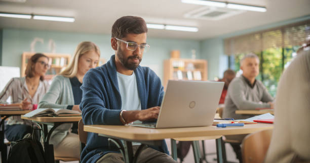 istock Attentive Indian Student Listening to Tutor and Writing Down Lecture on Laptop Computer in Class. Grown-Up Men and Women Getting Specialty Knowledge on a Part-Time Course in Modern College. 1759503585