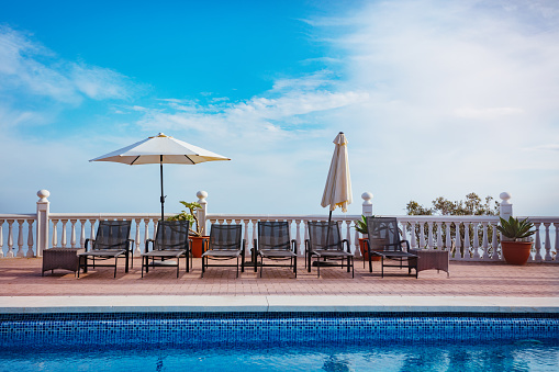 Swimming pool with set of chaise longs sun desk chairs, beach umbrellas casting shade over blue sky