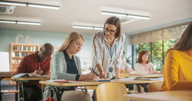 istock Helpful Young Teacher Talking with a Middle-Aged Female, Helping to Find a Solution for a Test Course Assignment. Multiethnic Women and Men of Different Age Acquiring New Academic Skills in Classroom 1759515907