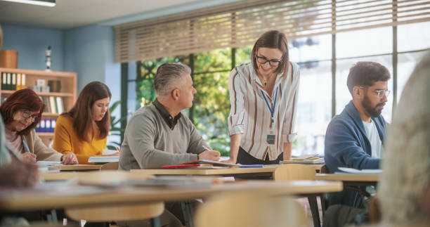 istock Helpful Young Teacher Talking with an Adult Man, Helping to Find a Solution for a Test Course Assignment. Multiethnic Women and Men of Different Age Acquiring New Academic Skills in Classroom 1759517011