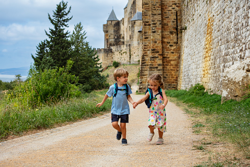 Twins, brother and sister explore historical city of Carcassonne together running along stone walls enjoying summer vacations in France