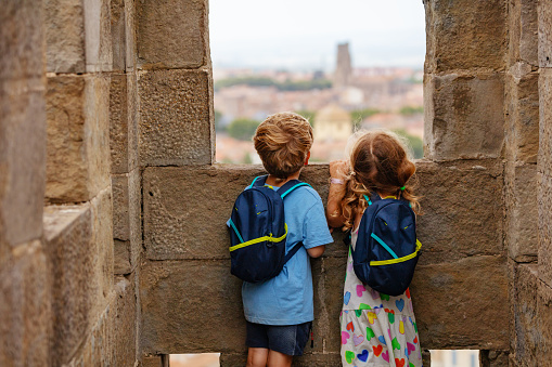 Happy tourists children with backpacks excited visiting stone towers of Carcassonne French fortress in Occitania, France on windy day