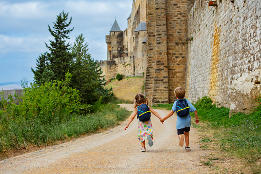 Kids do sightseeing running along huge walls of Carcassonne French fortified city in Occitania, South of France