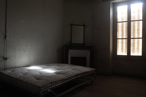 an old dusty quilt on a metal box spring in an abandoned room of an old house with closed shutters