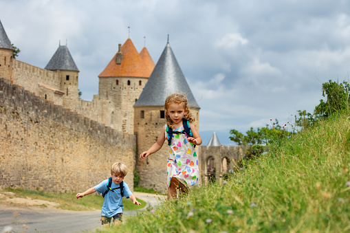 Little adventure seekers with backpacks run the hill over Carcassonne French fortified city in Occitania, France