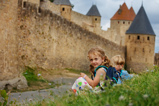 Twins, brother and sister explore historical city of Carcassonne together sitting along stone walls enjoying summer vacations in southern France