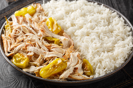 Shredded baked chicken fillet with peperoncini peppers served with rice close-up in a plate on the table. horizontal
