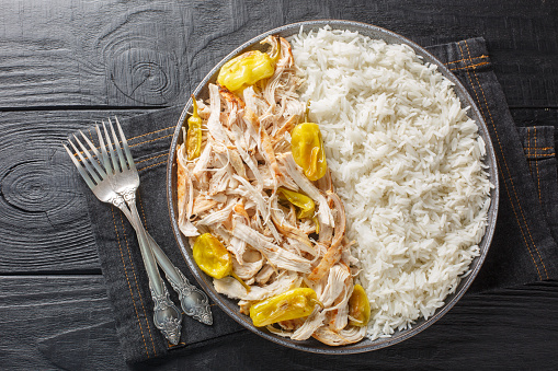 Shredded baked chicken fillet with peperoncini peppers served with rice close-up in a plate on the table. horizontal top view from above