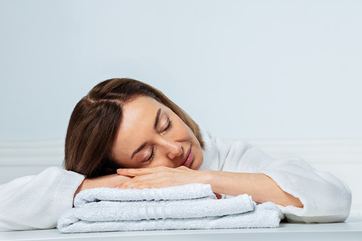 Close-up beauty portrait of a woman in her prime, with a confident smile in housecoat sleeping calmly on bathroom towels