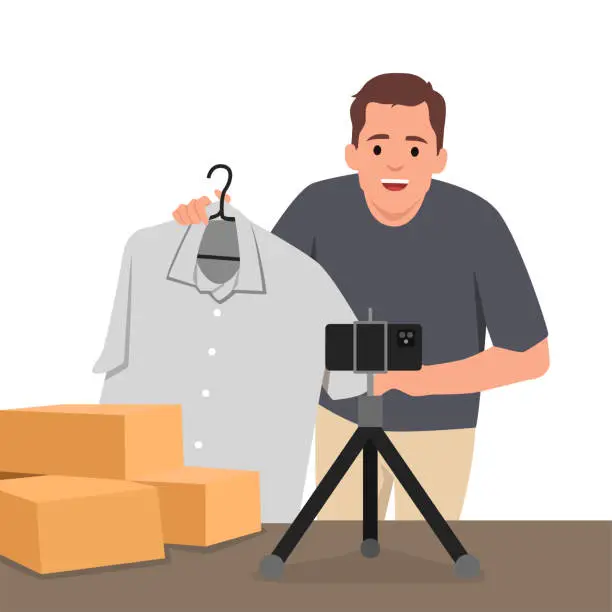 Vector illustration of Young man is showing clothes in front of smartphone live streaming at his shop. Live online selling.