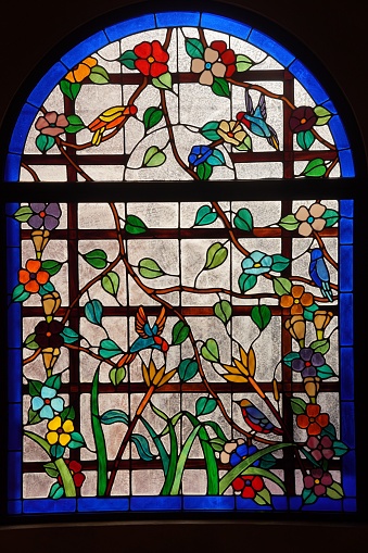 A beautiful stained glass window depicting colorful birds and flowers, set against a muted brick wall