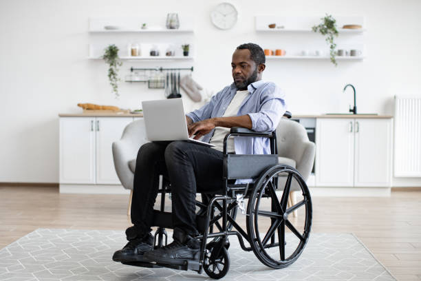 istock Man in wheelchair staying with laptop in open-plan kitchen 1759612248