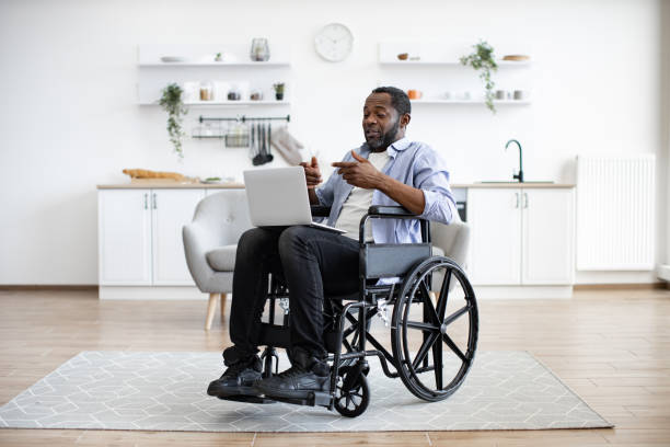 istock Man in wheelchair having video call on computer in apartment 1759612252