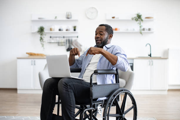 istock Man in wheelchair having video call on computer in apartment 1759612258