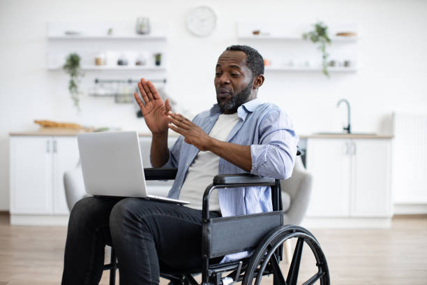 istock Man in wheelchair having video call on computer in apartment 1759612263