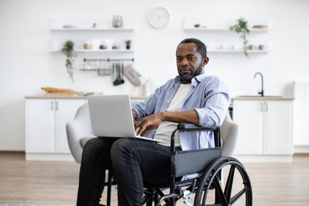 istock Man in wheelchair with laptop computer in apartment 1759612822