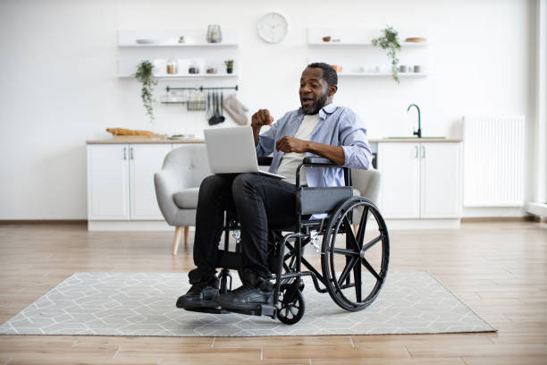 istock Man in wheelchair having video call on computer in apartment 1759613345