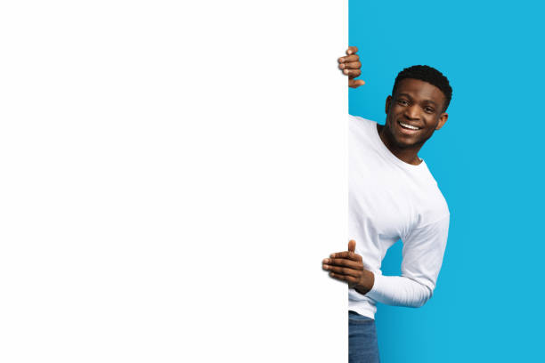 istock Cheerful african guy standing by white blank advertising board 1759618291