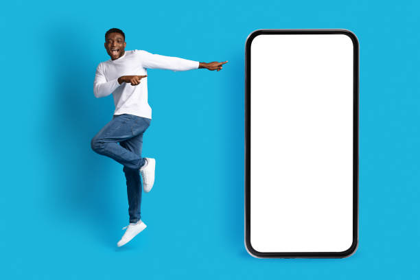 istock Positive happy black guy jumping next to big phone, mockup 1759619358