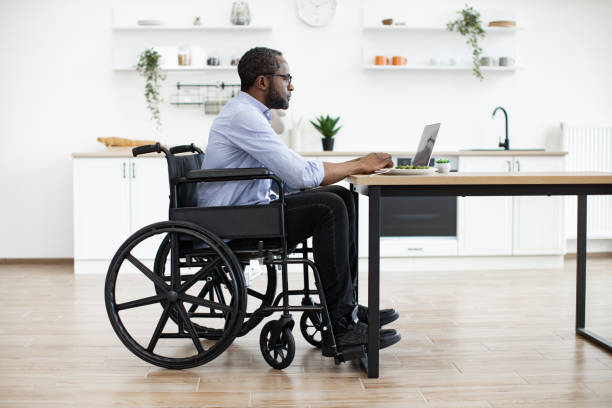 istock Male in wheelchair using laptop at desk in bright kitchen 1759623643