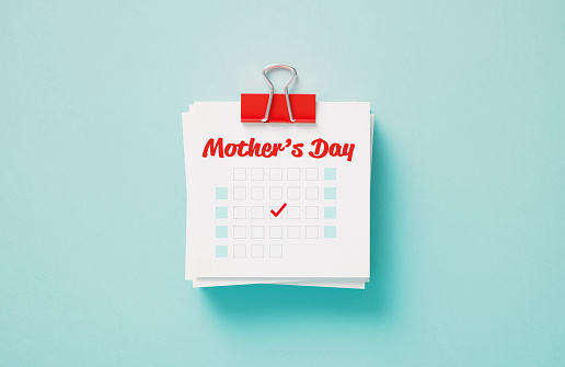 Mother's Day reminder held by a red paper clip on blue background. Horizontal composition with copy space. Calendar and reminder concept.