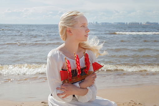 Blonde woman with red sail boat against sea beach and sky